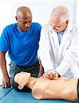 Mature doctor teaching an adult student how to perform CPR, using a dummy.