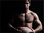 one caucasian sexy topless man portrait holding a rugby ball on studio black background