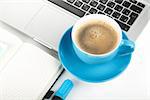 Blue coffee cup, laptop and office supplies. Closeup on white background