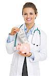 Smiling doctor woman putting dollars banknote in piggy bank