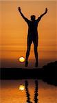 Silhouette woman jumping against orange sunset with reflection in water