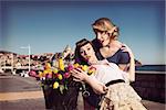 portrait of two fashion women with vintage style in funny pose near basket of the bicycle with some colourful flowers near the sea in vintage color