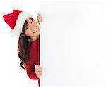 Santa girl peeking from behind blank sign billboard. Advertising photo of young smiling Christmas woman in Santa hat showing paper sign. Asian female model isolated on white background.