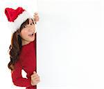 Santa girl peeking from behind blank sign billboard. Advertising photo of young surprised Christmas woman in Santa hat showing paper sign. Asian female model isolated on white background.