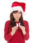 Christmas Gift - Asian woman looking at small gift disappointed and unhappy. Young woman in Santa hat. Funny cute photo of Asian woman isolated on white background.
