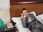 Smiling business woman laying on bed talking phone in hotel room