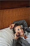 Business woman laying on bed in hotel room and talking cell phone