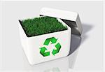 a small quantity of green grass is contained into a white uncovered box with a recycling symbol printed on its front side, on a white background.