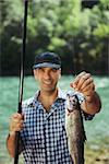 mid adult fisherman on holidays on river, relaxing and fishing trout. Focus on fish