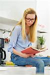 Teenager girl reading book in kitchen