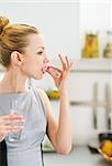 Young woman eating pill in kitchen