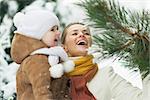 Happy mother and baby playing with snow on branch