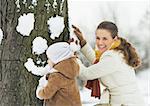 Happy mother and baby making face for tree using snow