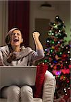 Happy young woman with laptop near christmas tree rejoicing