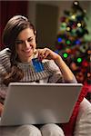 Smiling young woman with laptop and credit card near christmas tree