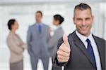 Smiling manager showing thumb up with employees in background in bright office