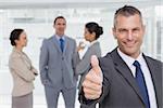 Cheerful manager showing thumb up with employees in background in bright office