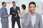 Businesswoman on the phone while colleagues talking in bright office