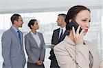 Businesswoman on the phone while colleagues talking together in bright office