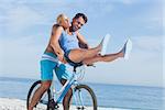 Happy man giving girlfriend a lift on his crossbar of bike on the beach