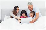 Smiling family lying in bed using their laptop at home