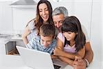 Smiling family sitting in kitchen using their laptop at home