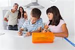 Siblings drawing together in kitchen with their parents smiling at home