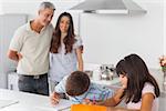 Cute siblings drawing together in kitchen with their parents smiling at home