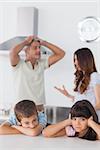 Unhappy siblings sitting in kitchen with their parents who are arguing loudly at home