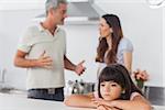Couple having dispute in front of their unsmiling daughter sitting in kitchen at home