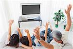 Family raising their arms in front of television at home