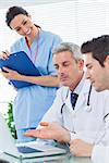 Smiling nurse listening to doctors talking about something on their laptop in medical office