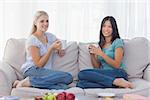 Friends drinking coffee together and smiling at camera at home on couch