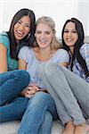 Friends laughing together and looking at camera at home on the couch