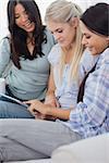 Happy friends using digital tablet together at home on couch