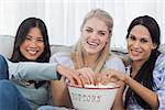Friends sharing bowl of popcorn and watching tv at home on couch