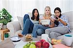 Friends sharing bowl of popcorn and watching television at home on couch