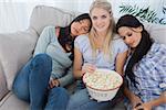 Friends dozing on blonde friends shoulders eating popcorn at home on couch