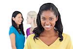 Smiling dark woman looking at camera with two women behind her on white background