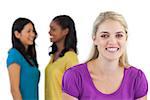 Smiling blonde woman looking at camera with two women behind her on white background