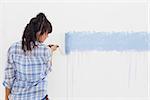 Woman painting wall blue with paint roller on blank wall