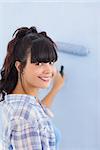 Cute woman painting wall blue and smiling at camera in new home