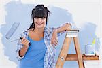 Woman holding paint roller leaning on ladder smiling at camera