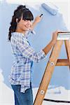 Woman using paint roller smiling at camera painting wall in blue
