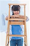 Happy woman holding paint roller leaning on ladder looking at camera