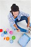 Happy woman sitting on floor with paint for decorating looking at camera