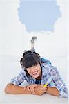 Brunette woman lying on floor holding paint brush winking at camera