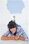 Attractive woman lying on floor holding paint brush smiling at camera