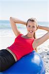 Fit blonde doing sit ups on exercise ball smiling at camera on the beach