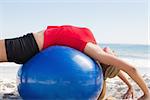 Fit blonde stretching back on exercise ball on the beach